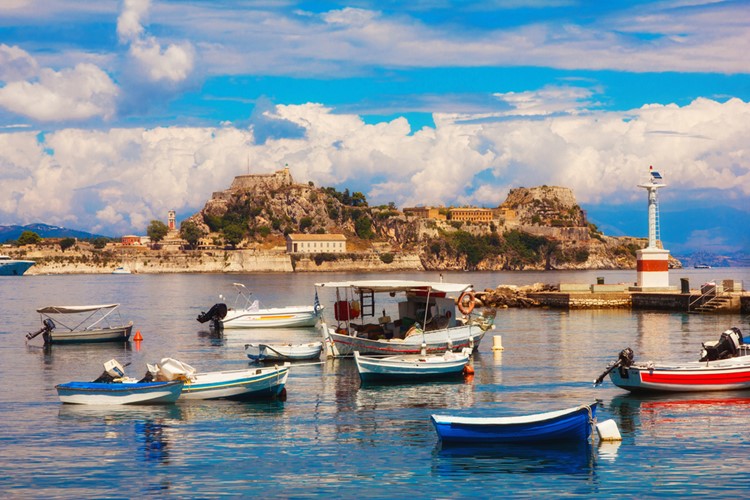 km travel_Fishing boats in Corfu marina with the Old Byzantine Fortress in the background